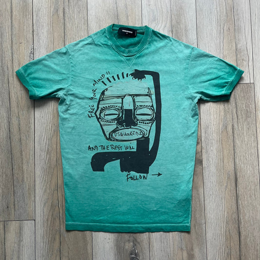 Dsquared2 SS2015 “Free Your Mind” T-shirt is a turquoise cotton tee with a washed, faded finish and tonal variation across the fabric. The front features a black Basquiat-inspired figure with “Free Your Mind and the Rest Will Follow” text in a contrasting design. The piece is made in Italy and includes darker tonal hems with a lighter center fade for a worn effect.
