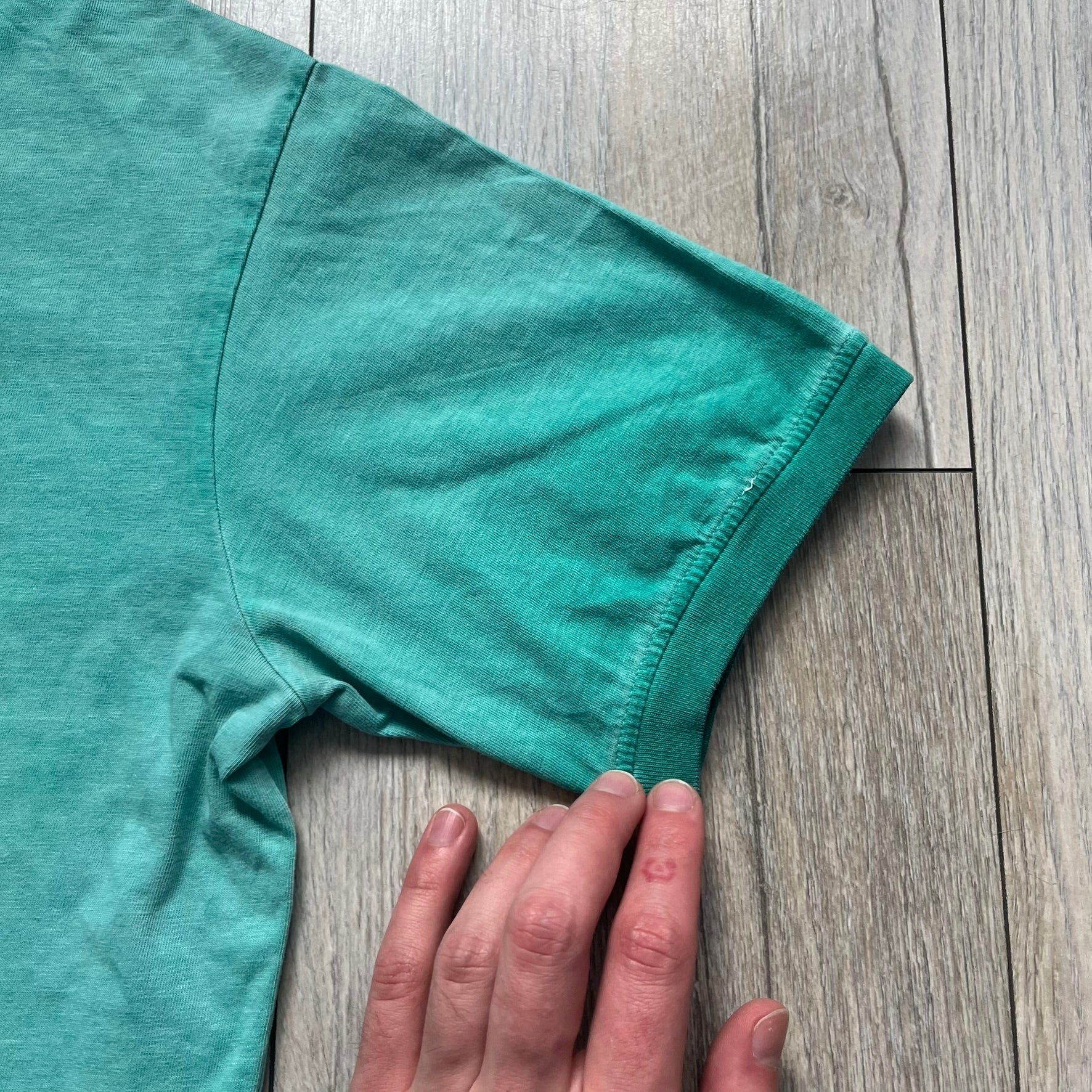 Dsquared2 SS2015 “Free Your Mind” T-shirt is a turquoise cotton tee with a washed, faded finish and tonal variation across the fabric. The front features a black Basquiat-inspired figure with “Free Your Mind and the Rest Will Follow” text in a contrasting design. The piece is made in Italy and includes darker tonal hems with a lighter center fade for a worn effect.