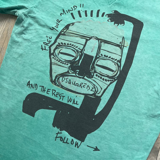 Dsquared2 SS2015 “Free Your Mind” T-shirt is a turquoise cotton tee with a washed, faded finish and tonal variation across the fabric. The front features a black Basquiat-inspired figure with “Free Your Mind and the Rest Will Follow” text in a contrasting design. The piece is made in Italy and includes darker tonal hems with a lighter center fade for a worn effect.