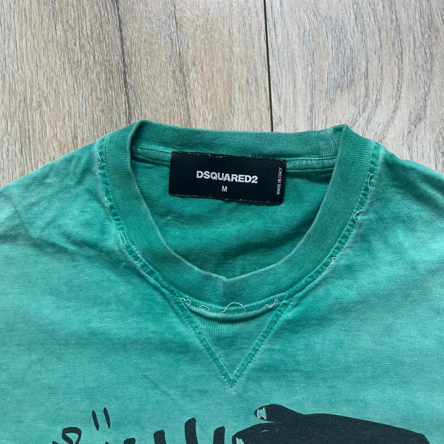 Dsquared2 SS2015 “Free Your Mind” T-shirt is a turquoise cotton tee with a washed, faded finish and tonal variation across the fabric. The front features a black Basquiat-inspired figure with “Free Your Mind and the Rest Will Follow” text in a contrasting design. The piece is made in Italy and includes darker tonal hems with a lighter center fade for a worn effect.