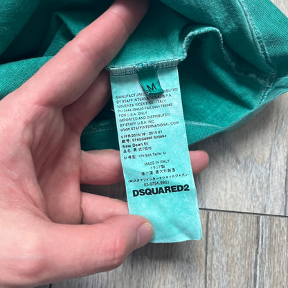 Dsquared2 SS2015 “Free Your Mind” T-shirt is a turquoise cotton tee with a washed, faded finish and tonal variation across the fabric. The front features a black Basquiat-inspired figure with “Free Your Mind and the Rest Will Follow” text in a contrasting design. The piece is made in Italy and includes darker tonal hems with a lighter center fade for a worn effect.