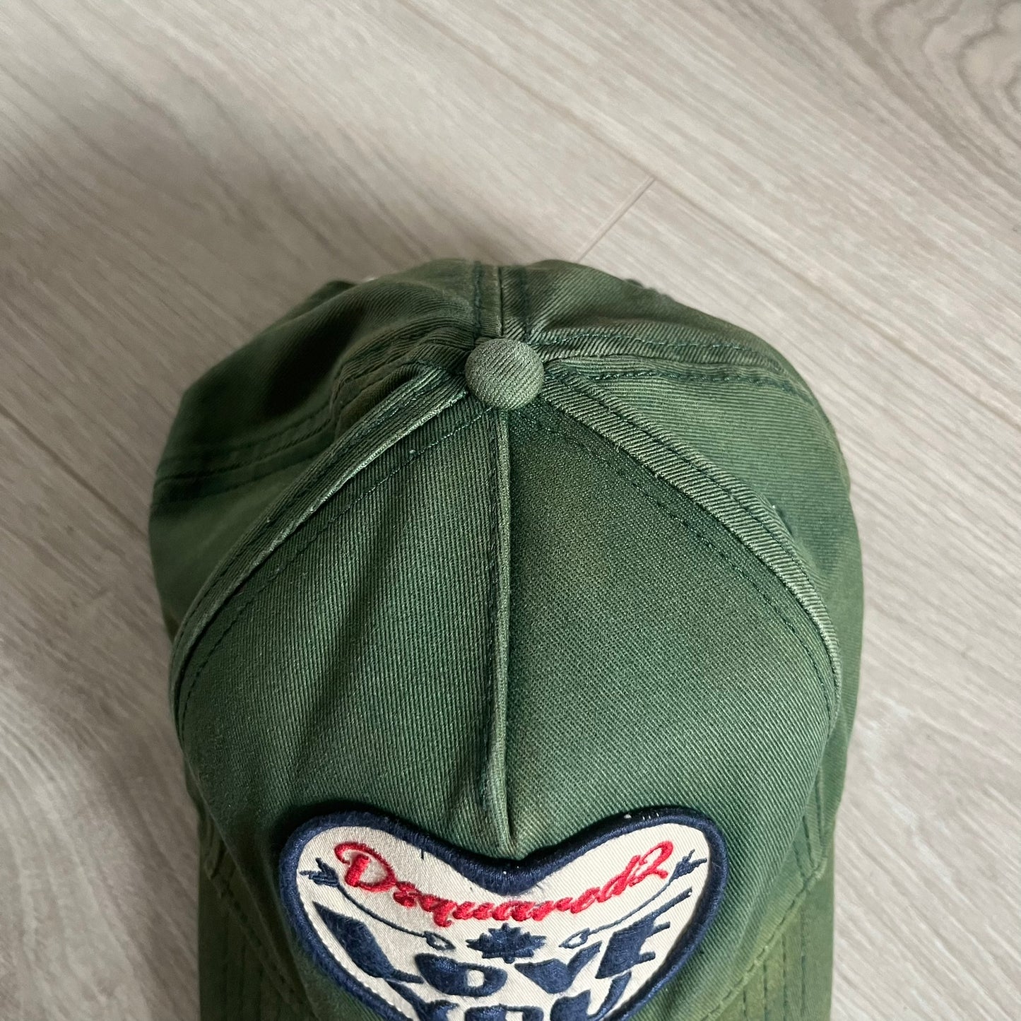 Green cap with a heart-shaped patch on a light wooden surface