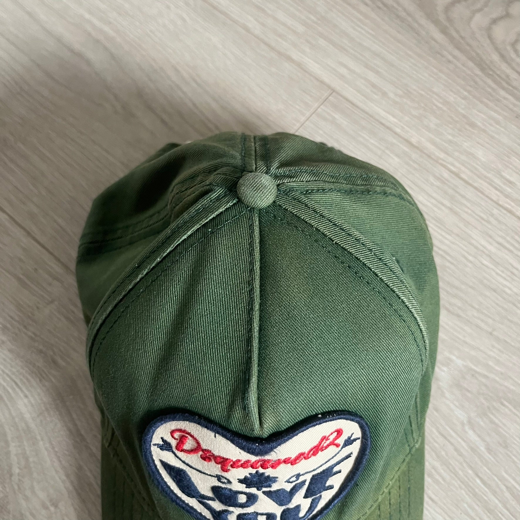 Green cap with a heart-shaped patch on a light wooden surface