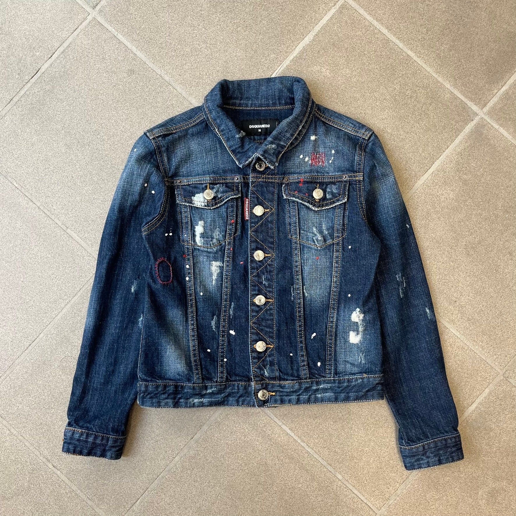 Dsquared2 SS15 Rebel Monkey Denim Jacket features a denim construction with two chest pockets on the front. The back has a large Rebel Monkey graphic in white, blue, and red, with black Dsquared2 text above it. The jacket includes intentional tears, paint splatters, and other distressed details. Made in Italy as part of the Dsquared2 collaboration with Basquiat.
