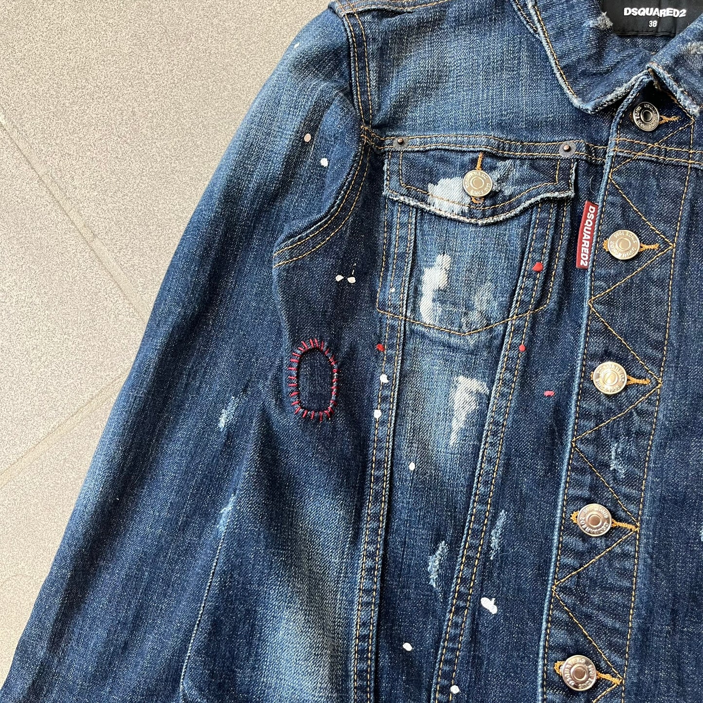 Dsquared2 SS15 Rebel Monkey Denim Jacket features a denim construction with two chest pockets on the front. The back has a large Rebel Monkey graphic in white, blue, and red, with black Dsquared2 text above it. The jacket includes intentional tears, paint splatters, and other distressed details. Made in Italy as part of the Dsquared2 collaboration with Basquiat.
