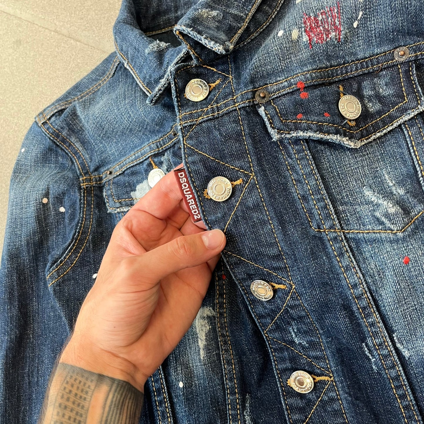 Dsquared2 SS15 Rebel Monkey Denim Jacket features a denim construction with two chest pockets on the front. The back has a large Rebel Monkey graphic in white, blue, and red, with black Dsquared2 text above it. The jacket includes intentional tears, paint splatters, and other distressed details. Made in Italy as part of the Dsquared2 collaboration with Basquiat.
