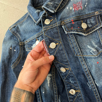 Dsquared2 SS15 Rebel Monkey Denim Jacket features a denim construction with two chest pockets on the front. The back has a large Rebel Monkey graphic in white, blue, and red, with black Dsquared2 text above it. The jacket includes intentional tears, paint splatters, and other distressed details. Made in Italy as part of the Dsquared2 collaboration with Basquiat.
