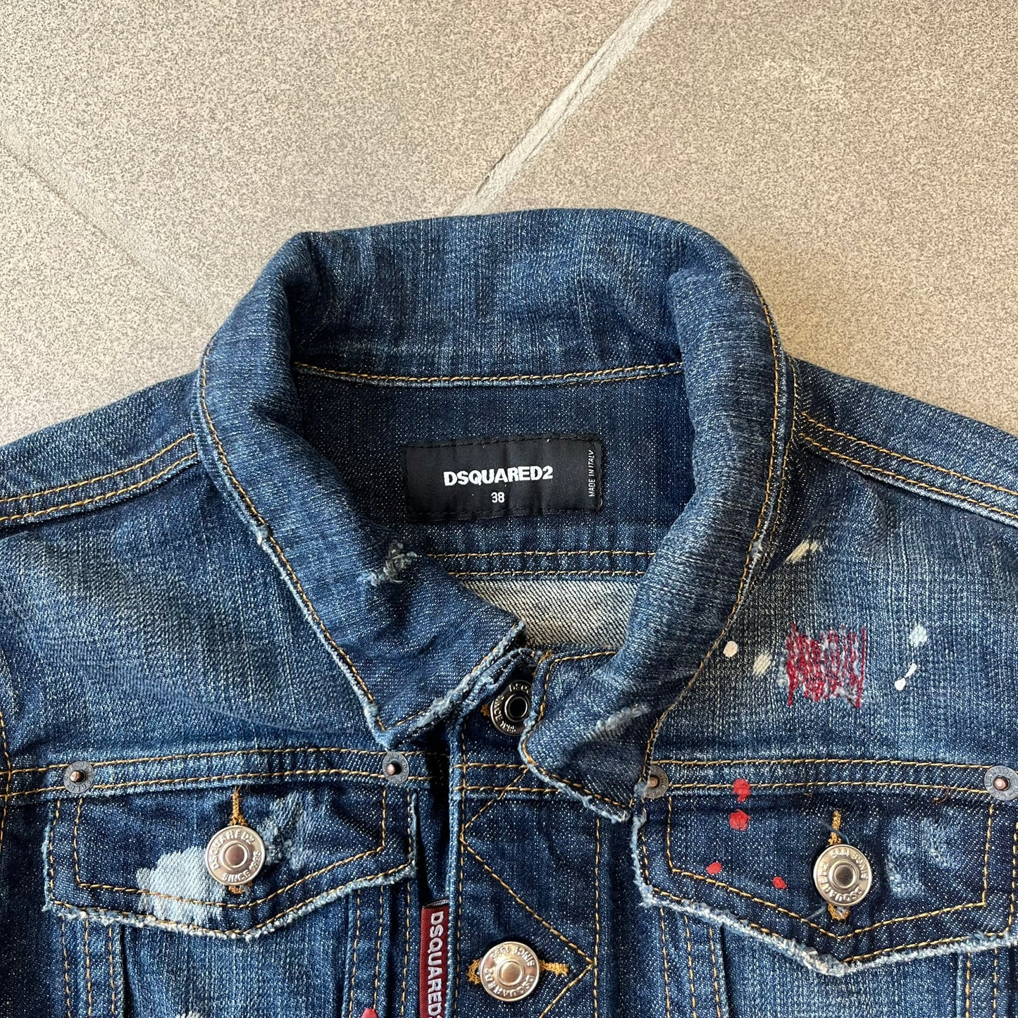 Dsquared2 SS15 Rebel Monkey Denim Jacket features a denim construction with two chest pockets on the front. The back has a large Rebel Monkey graphic in white, blue, and red, with black Dsquared2 text above it. The jacket includes intentional tears, paint splatters, and other distressed details. Made in Italy as part of the Dsquared2 collaboration with Basquiat.
