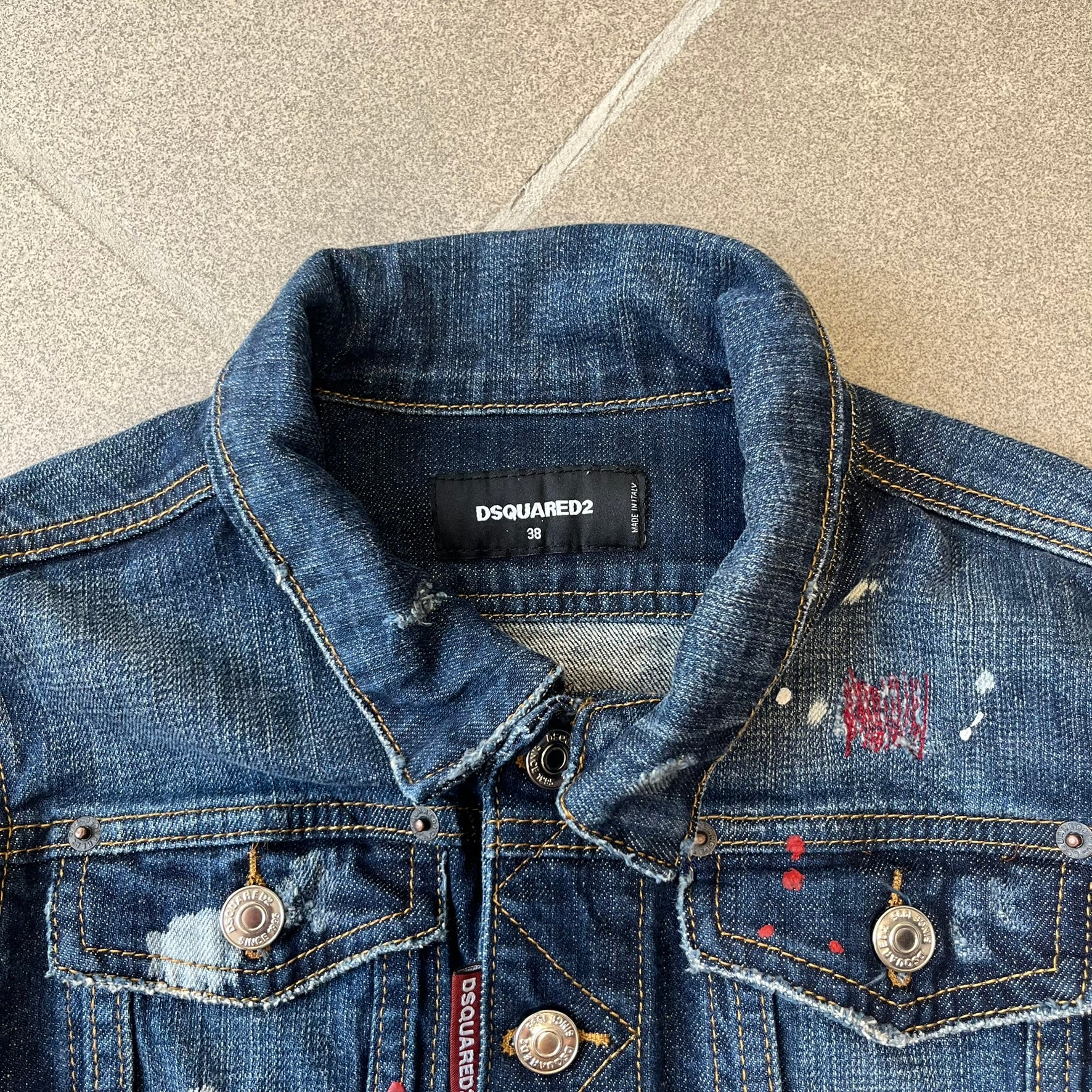 Dsquared2 SS15 Rebel Monkey Denim Jacket features a denim construction with two chest pockets on the front. The back has a large Rebel Monkey graphic in white, blue, and red, with black Dsquared2 text above it. The jacket includes intentional tears, paint splatters, and other distressed details. Made in Italy as part of the Dsquared2 collaboration with Basquiat.
