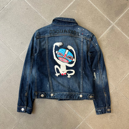Dsquared2 SS15 Rebel Monkey Denim Jacket features a denim construction with two chest pockets on the front. The back has a large Rebel Monkey graphic in white, blue, and red, with black Dsquared2 text above it. The jacket includes intentional tears, paint splatters, and other distressed details. Made in Italy as part of the Dsquared2 collaboration with Basquiat.
