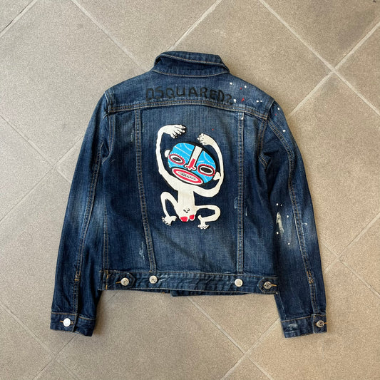 Dsquared2 SS15 Rebel Monkey Denim Jacket features a denim construction with two chest pockets on the front. The back has a large Rebel Monkey graphic in white, blue, and red, with black Dsquared2 text above it. The jacket includes intentional tears, paint splatters, and other distressed details. Made in Italy as part of the Dsquared2 collaboration with Basquiat.
