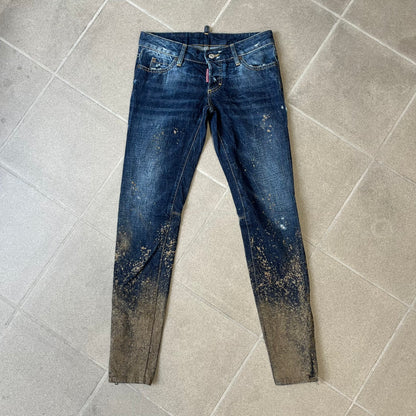 Dsquared2 SS2012 Mud Splash Jeans are runway bottoms from the Spring/Summer 2012 collection, made in Italy from 100% cotton. The jeans feature a deliberate two-tone design with a clean blue-denim upper section transitioning into a heavy brown “mud” effect on the lower half. They include branded buttons and rivets, a Dsquared2 back patch, and a small red maple leaf metal pin on the back pocket.