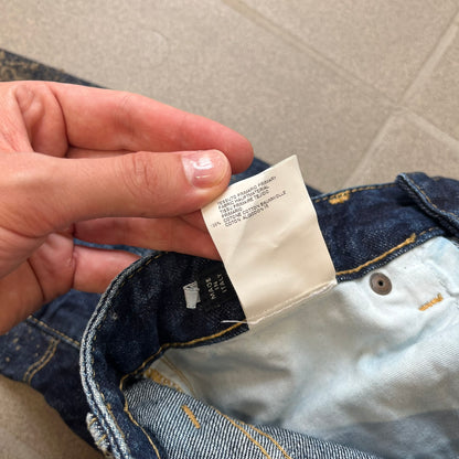 Dsquared2 SS2012 Mud Splash Jeans are runway bottoms from the Spring/Summer 2012 collection, made in Italy from 100% cotton. The jeans feature a deliberate two-tone design with a clean blue-denim upper section transitioning into a heavy brown “mud” effect on the lower half. They include branded buttons and rivets, a Dsquared2 back patch, and a small red maple leaf metal pin on the back pocket.