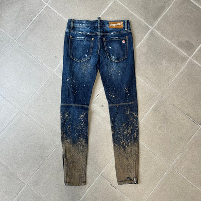 Dsquared2 SS2012 Mud Splash Jeans are runway bottoms from the Spring/Summer 2012 collection, made in Italy from 100% cotton. The jeans feature a deliberate two-tone design with a clean blue-denim upper section transitioning into a heavy brown “mud” effect on the lower half. They include branded buttons and rivets, a Dsquared2 back patch, and a small red maple leaf metal pin on the back pocket.