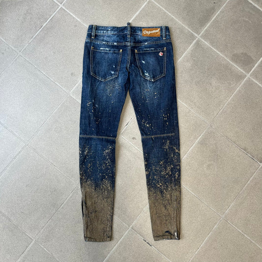Dsquared2 SS2012 Mud Splash Jeans are runway bottoms from the Spring/Summer 2012 collection, made in Italy from 100% cotton. The jeans feature a deliberate two-tone design with a clean blue-denim upper section transitioning into a heavy brown “mud” effect on the lower half. They include branded buttons and rivets, a Dsquared2 back patch, and a small red maple leaf metal pin on the back pocket.