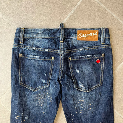 Dsquared2 SS2012 Mud Splash Jeans are runway bottoms from the Spring/Summer 2012 collection, made in Italy from 100% cotton. The jeans feature a deliberate two-tone design with a clean blue-denim upper section transitioning into a heavy brown “mud” effect on the lower half. They include branded buttons and rivets, a Dsquared2 back patch, and a small red maple leaf metal pin on the back pocket.
