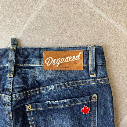 Dsquared2 SS2012 Mud Splash Jeans are runway bottoms from the Spring/Summer 2012 collection, made in Italy from 100% cotton. The jeans feature a deliberate two-tone design with a clean blue-denim upper section transitioning into a heavy brown “mud” effect on the lower half. They include branded buttons and rivets, a Dsquared2 back patch, and a small red maple leaf metal pin on the back pocket.