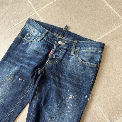 Dsquared2 SS2012 Mud Splash Jeans are runway bottoms from the Spring/Summer 2012 collection, made in Italy from 100% cotton. The jeans feature a deliberate two-tone design with a clean blue-denim upper section transitioning into a heavy brown “mud” effect on the lower half. They include branded buttons and rivets, a Dsquared2 back patch, and a small red maple leaf metal pin on the back pocket.