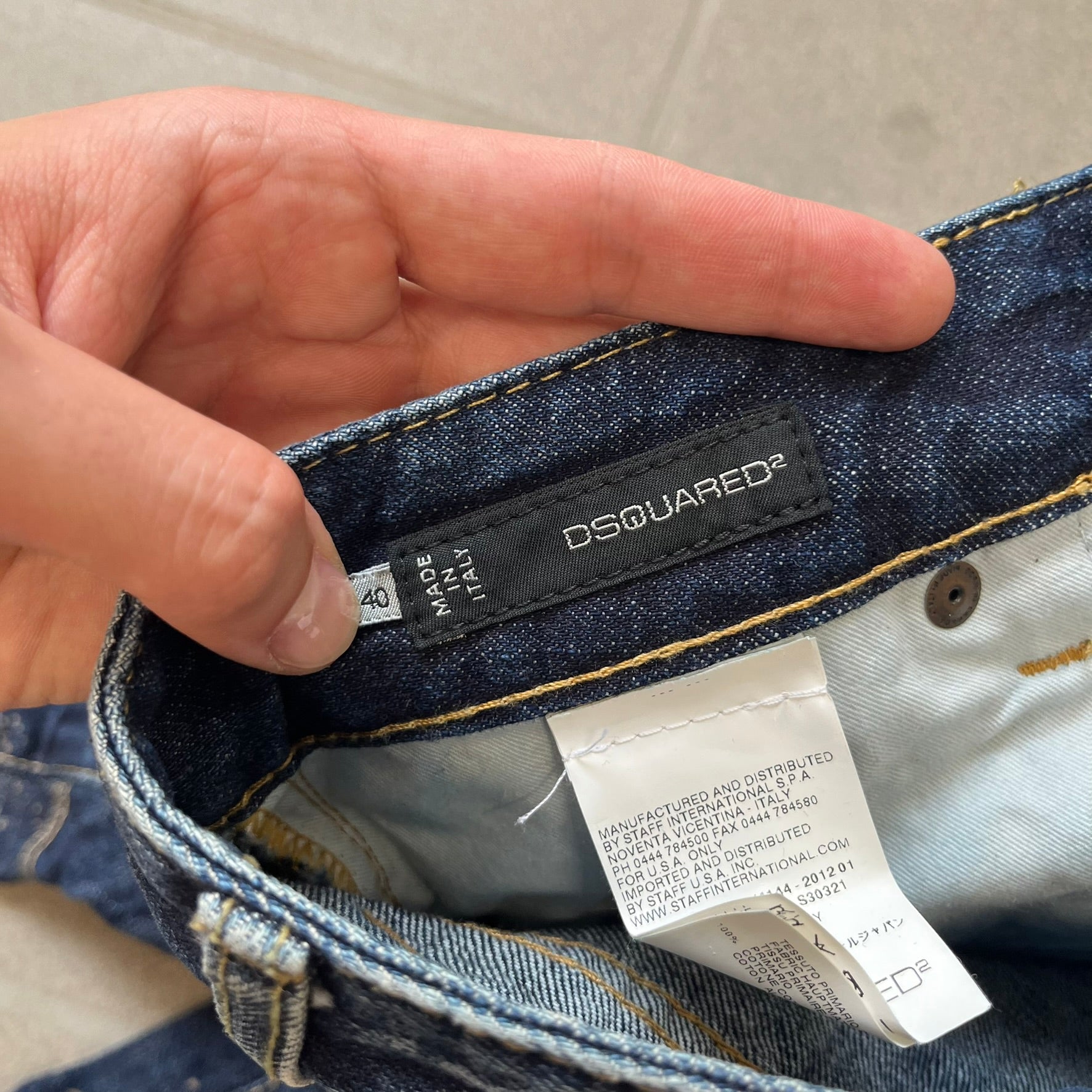 Dsquared2 SS2012 Mud Splash Jeans are runway bottoms from the Spring/Summer 2012 collection, made in Italy from 100% cotton. The jeans feature a deliberate two-tone design with a clean blue-denim upper section transitioning into a heavy brown “mud” effect on the lower half. They include branded buttons and rivets, a Dsquared2 back patch, and a small red maple leaf metal pin on the back pocket.