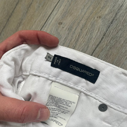 Dsquared2 SS2012 White Mud Jeans are runway pieces from the Spring/Summer 2012 collection, made in Italy from 98% cotton and 2% elastane. The jeans feature a deliberate two-tone design with a clean white upper section transitioning into a heavy brown “mud” effect on the lower half. They include branded buttons and rivets, a Dsquared2 front patch, and a small red maple leaf metal pin on the back pocket. The leg opening measures approximately 17 cm, with a slightly stretchy slim fit construction.
