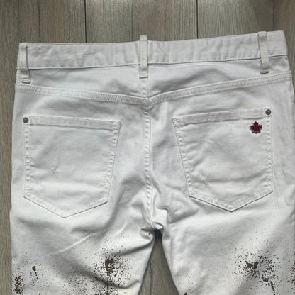 Dsquared2 SS2012 White Mud Jeans are runway pieces from the Spring/Summer 2012 collection, made in Italy from 98% cotton and 2% elastane. The jeans feature a deliberate two-tone design with a clean white upper section transitioning into a heavy brown “mud” effect on the lower half. They include branded buttons and rivets, a Dsquared2 front patch, and a small red maple leaf metal pin on the back pocket. The leg opening measures approximately 17 cm, with a slightly stretchy slim fit construction.