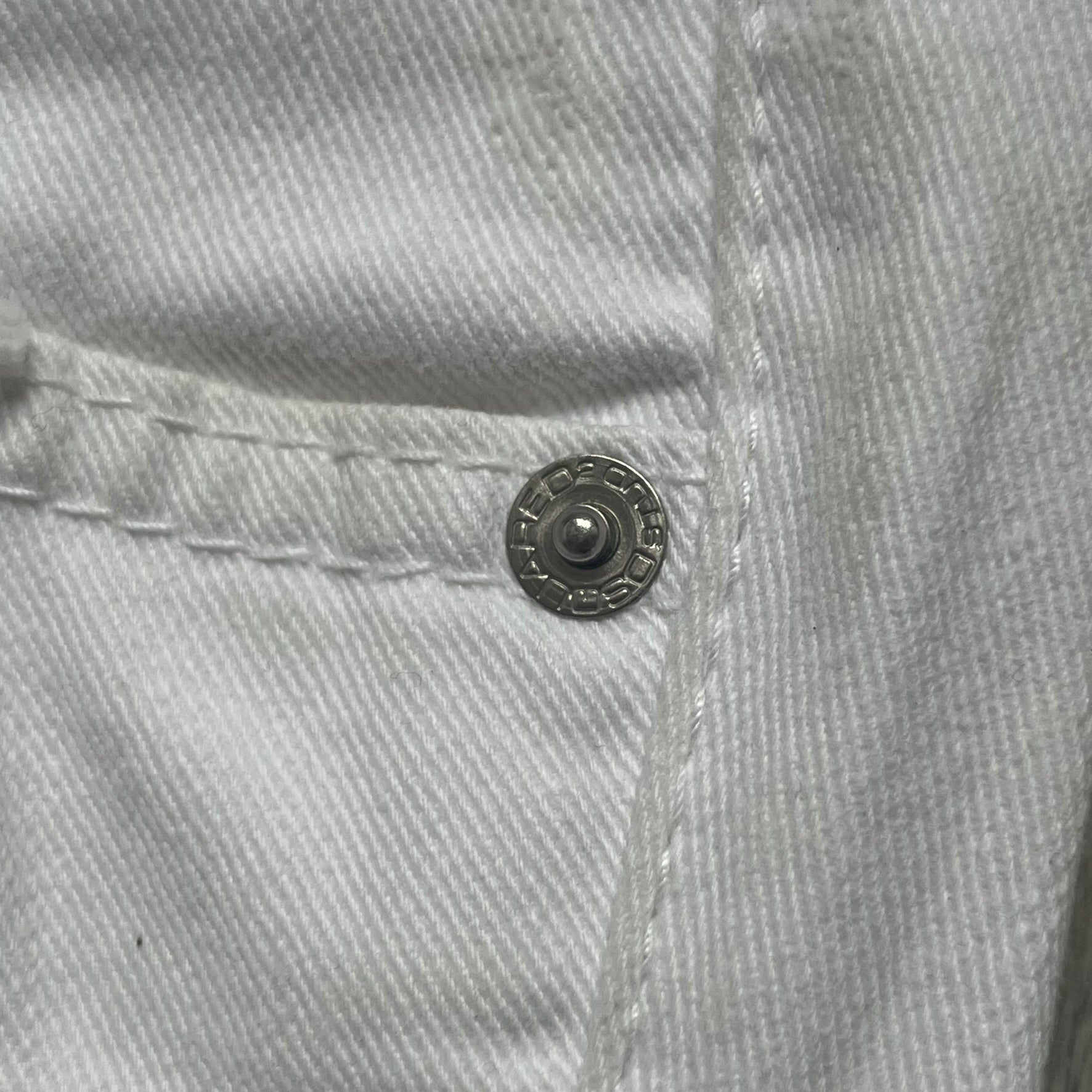 Dsquared2 SS2012 White Mud Jeans are runway pieces from the Spring/Summer 2012 collection, made in Italy from 98% cotton and 2% elastane. The jeans feature a deliberate two-tone design with a clean white upper section transitioning into a heavy brown “mud” effect on the lower half. They include branded buttons and rivets, a Dsquared2 front patch, and a small red maple leaf metal pin on the back pocket. The leg opening measures approximately 17 cm, with a slightly stretchy slim fit construction.