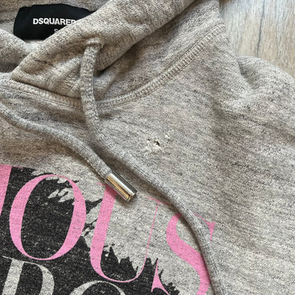 Dsquared2 Vicious Bros SS2019 Hoodie is a grey cotton hoodie made in Italy. It features a hood with drawstring fastening, long sleeves, and ribbed cuffs and hem. The front includes a printed graphic of two outlined figures with a small Dsquared2 logo and pink “Vicious Bros” text above them. The hoodie has intentional distressing throughout the fabric.
