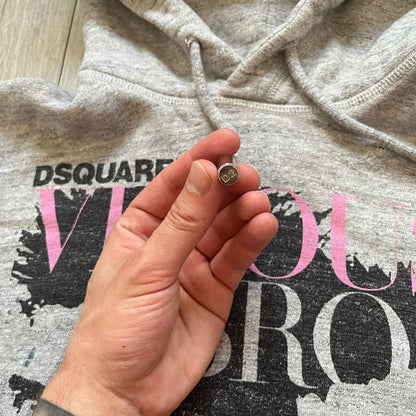 Dsquared2 Vicious Bros SS2019 Hoodie is a grey cotton hoodie made in Italy. It features a hood with drawstring fastening, long sleeves, and ribbed cuffs and hem. The front includes a printed graphic of two outlined figures with a small Dsquared2 logo and pink “Vicious Bros” text above them. The hoodie has intentional distressing throughout the fabric.
