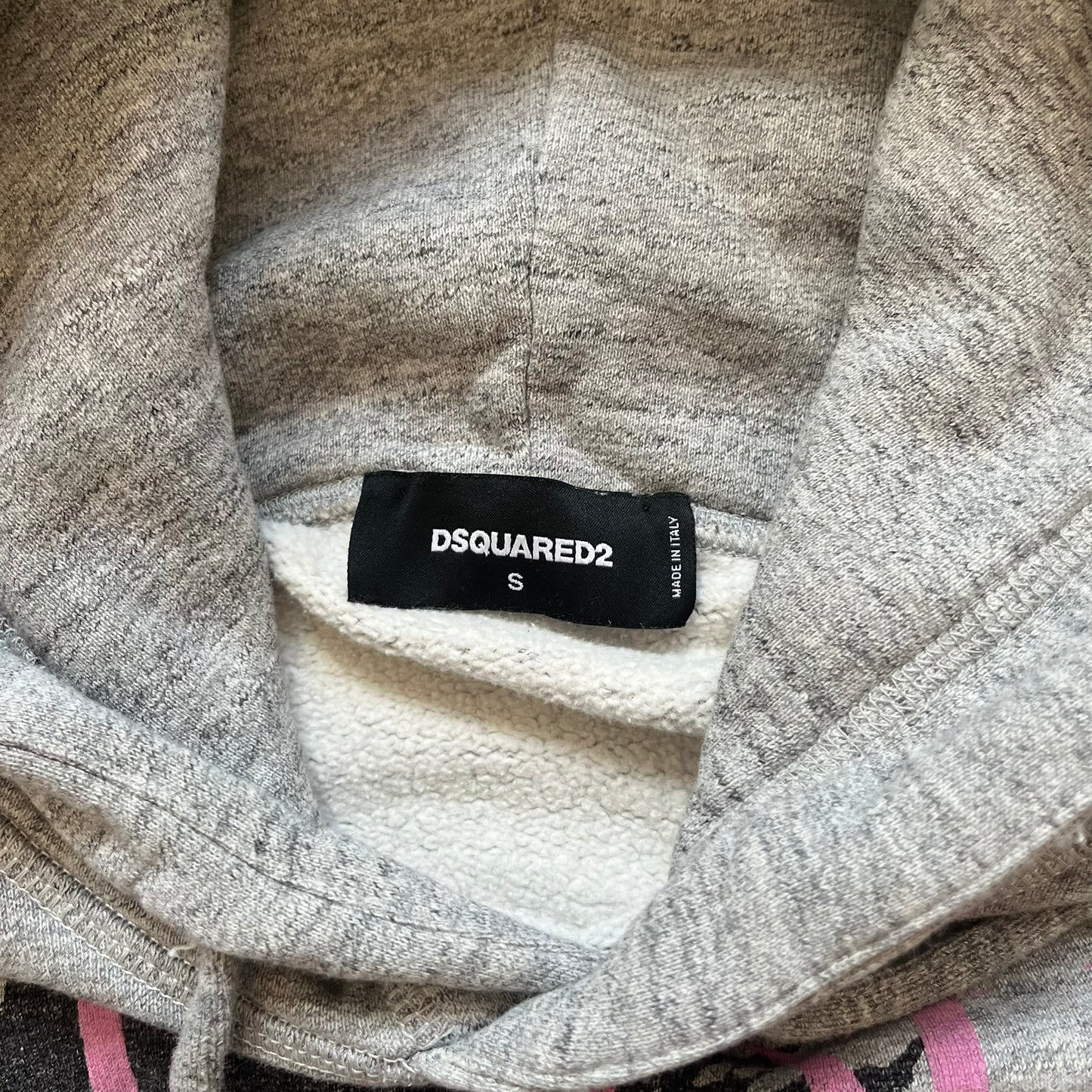 Dsquared2 Vicious Bros SS2019 Hoodie is a grey cotton hoodie made in Italy. It features a hood with drawstring fastening, long sleeves, and ribbed cuffs and hem. The front includes a printed graphic of two outlined figures with a small Dsquared2 logo and pink “Vicious Bros” text above them. The hoodie has intentional distressing throughout the fabric.
