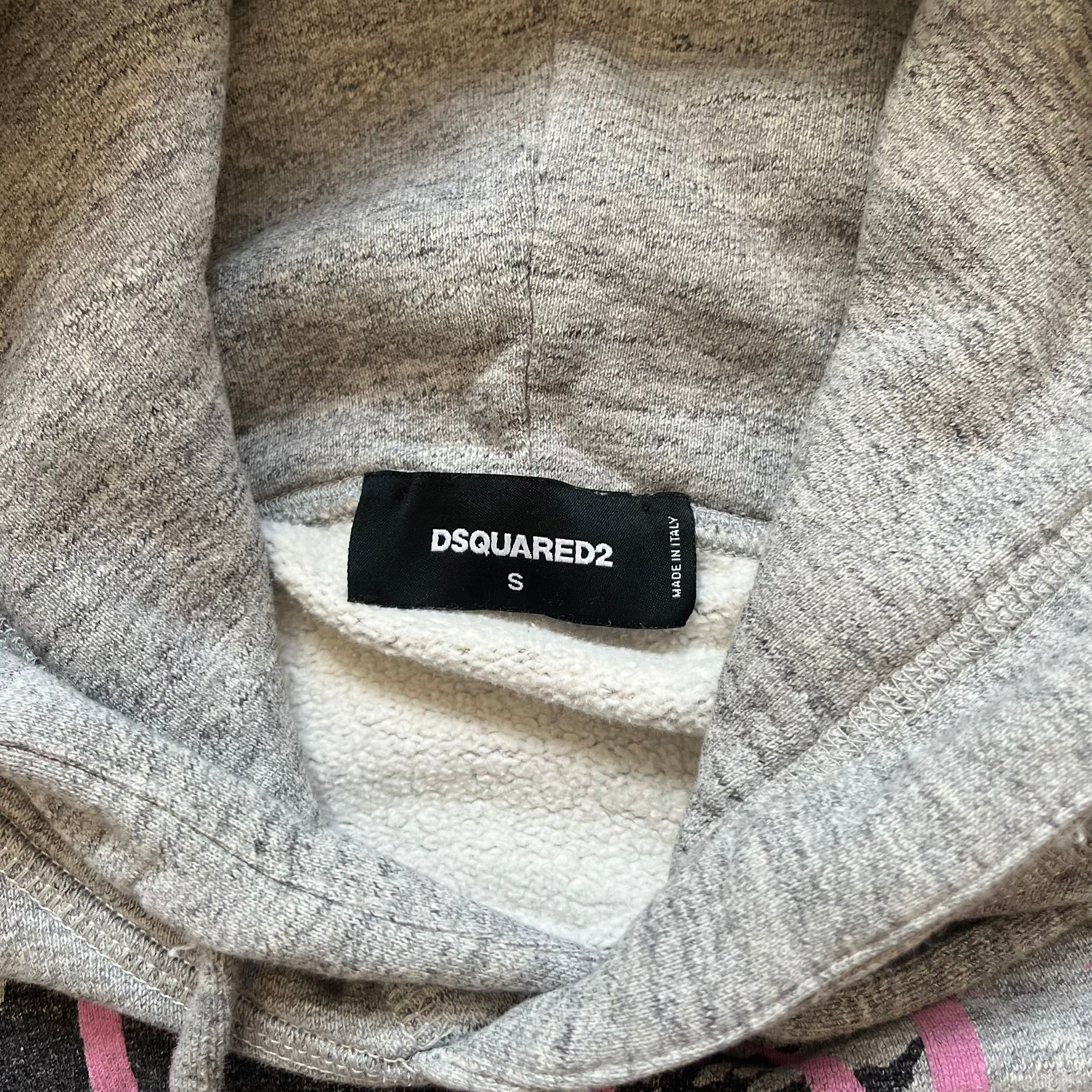 Dsquared2 Vicious Bros SS2019 Hoodie is a grey cotton hoodie made in Italy. It features a hood with drawstring fastening, long sleeves, and ribbed cuffs and hem. The front includes a printed graphic of two outlined figures with a small Dsquared2 logo and pink “Vicious Bros” text above them. The hoodie has intentional distressing throughout the fabric.
