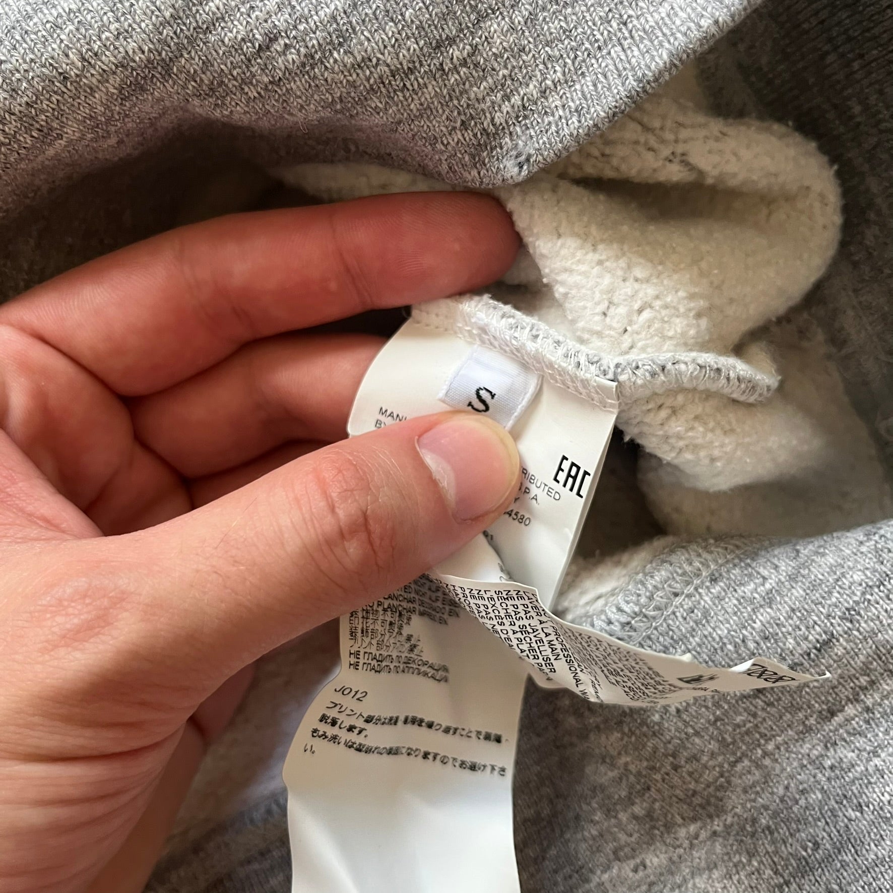 Dsquared2 Vicious Bros SS2019 Hoodie is a grey cotton hoodie made in Italy. It features a hood with drawstring fastening, long sleeves, and ribbed cuffs and hem. The front includes a printed graphic of two outlined figures with a small Dsquared2 logo and pink “Vicious Bros” text above them. The hoodie has intentional distressing throughout the fabric.
