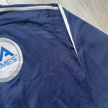 EA Sports 2000s Track Jacket is a navy track jacket with a full white zip closure, white two stripes running down both sleeves, and a fold-down collar. The back features a large stitched EA GAMES circular logo patch.&nbsp;