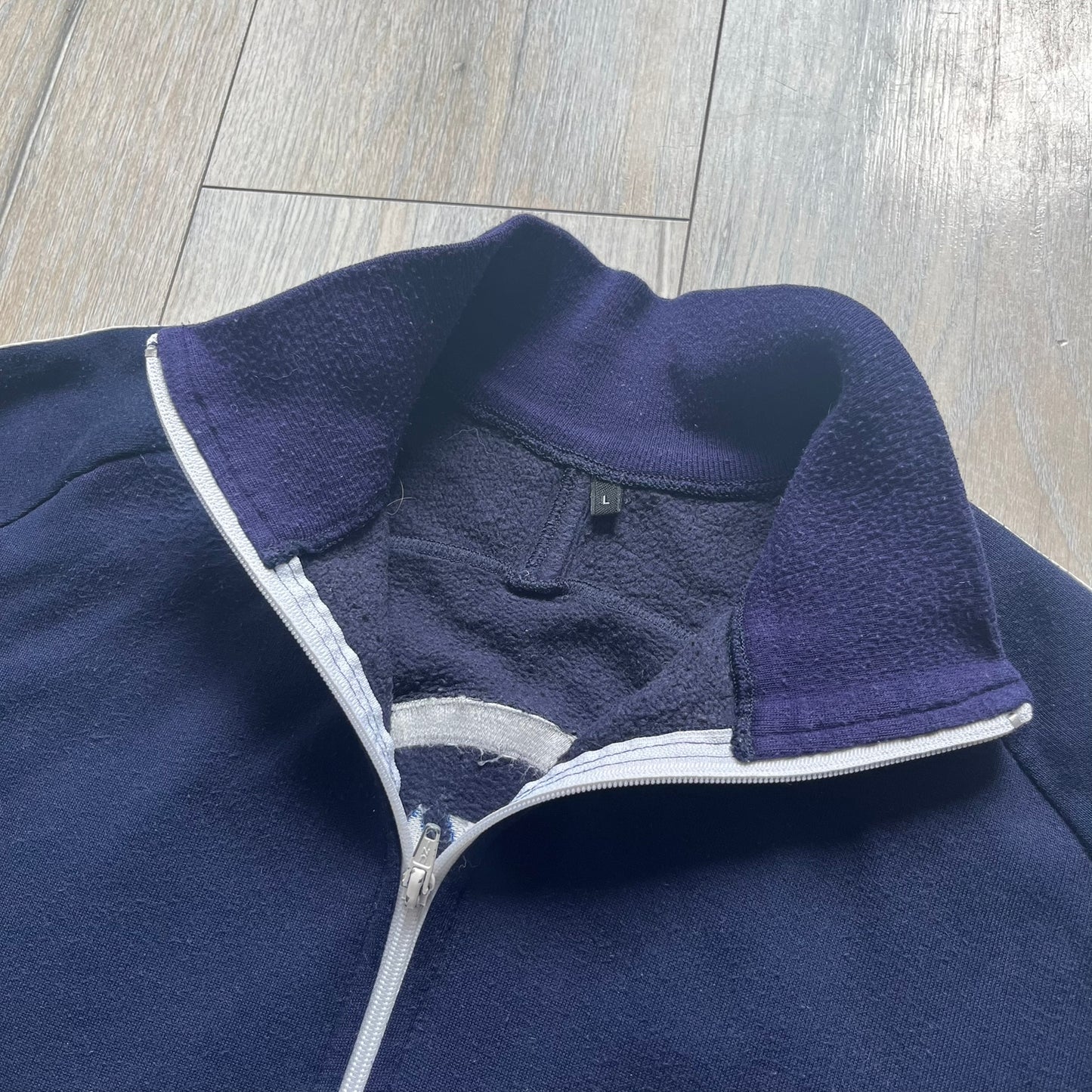 EA Sports 2000s Track Jacket is a navy track jacket with a full white zip closure, white two stripes running down both sleeves, and a fold-down collar. The back features a large stitched EA GAMES circular logo patch.&nbsp;