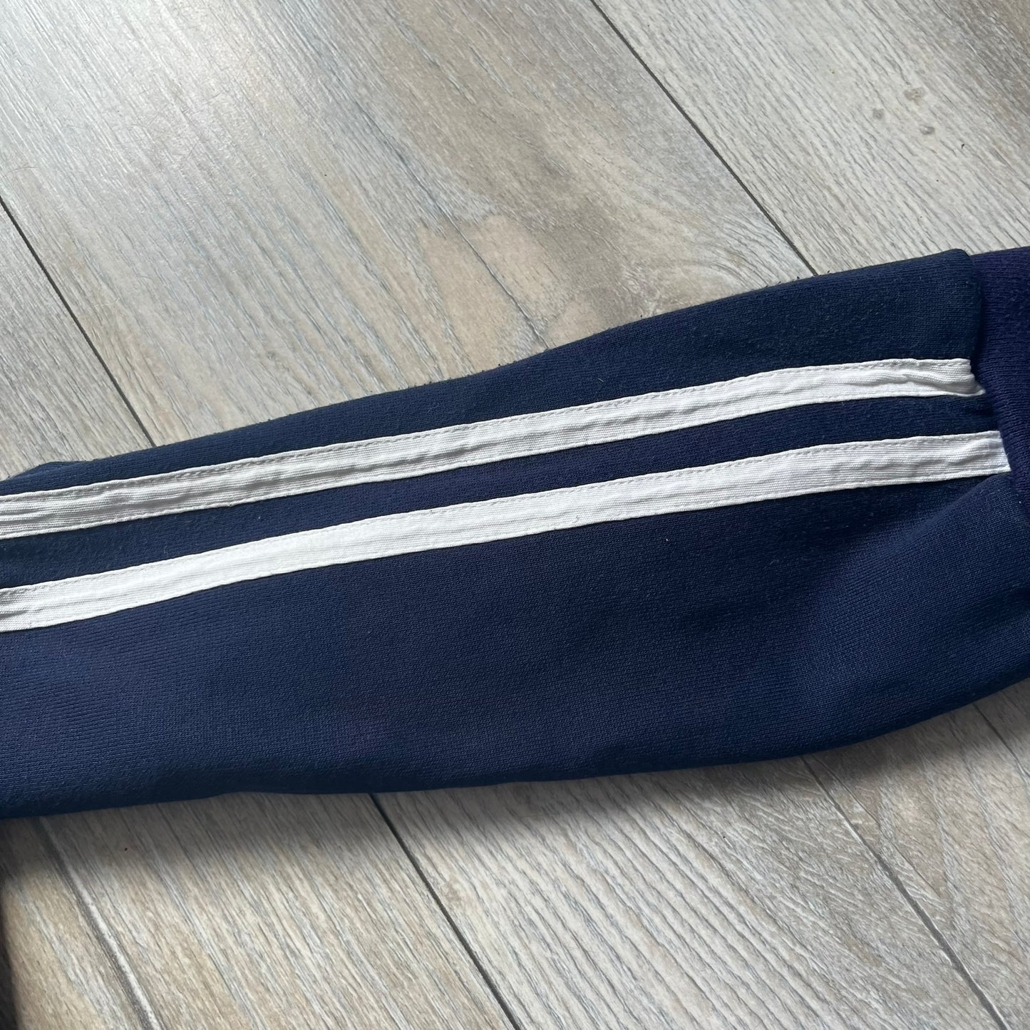 EA Sports 2000s Track Jacket is a navy track jacket with a full white zip closure, white two stripes running down both sleeves, and a fold-down collar. The back features a large stitched EA GAMES circular logo patch.&nbsp;