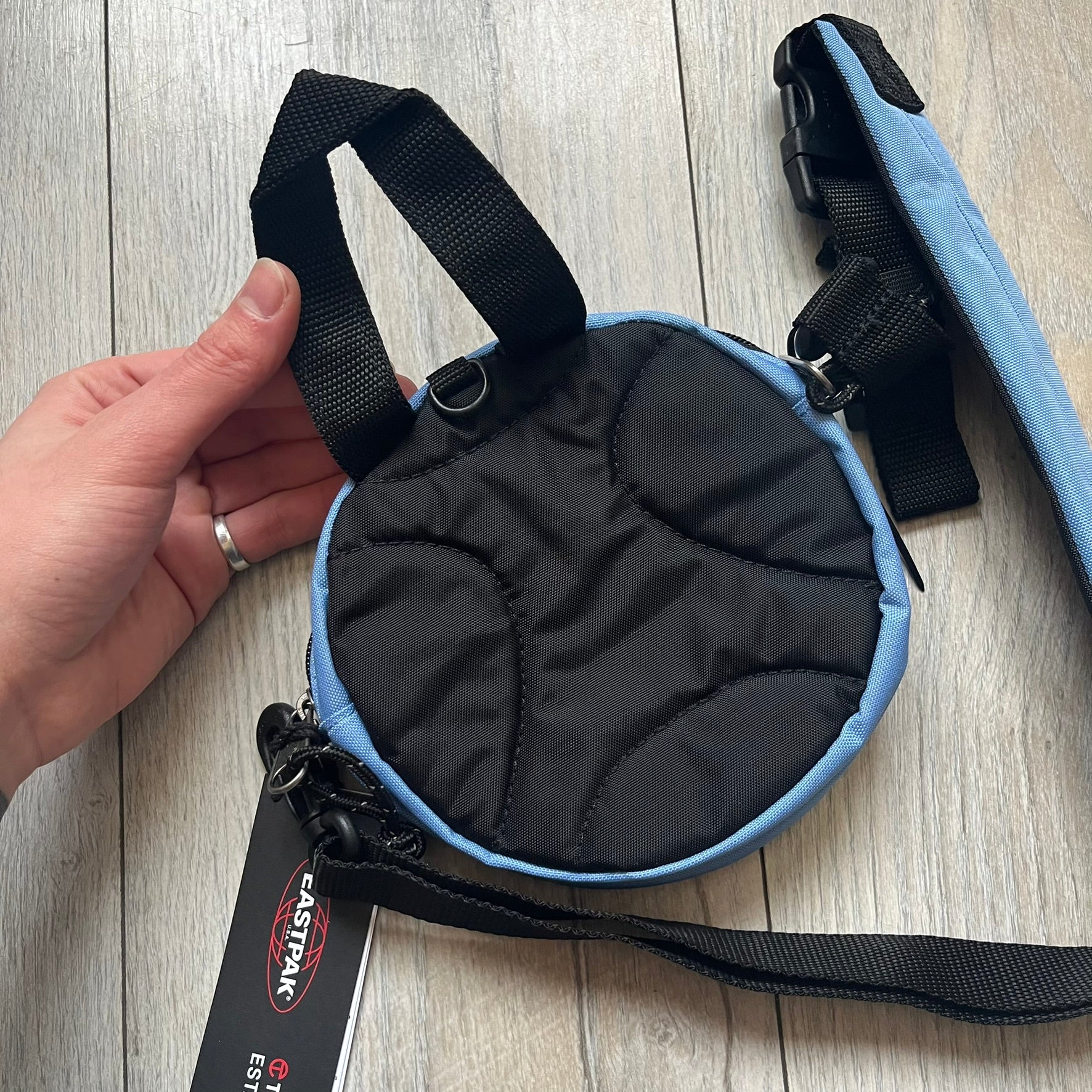 Eastpak x Telfar Circle Blue Shoulder Bag is crafted from polyester tactical canvas in a Cerulean colorway with black-tone hardware. The bag features woven hand straps, a removable and adjustable padded shoulder strap for crossbody or waist wear, and an embossed Telfar logo on the exterior. Released for SS24 on 06/14/2024 with a retail price of $110, the interior includes zip pockets and mesh compartments for organized storage.