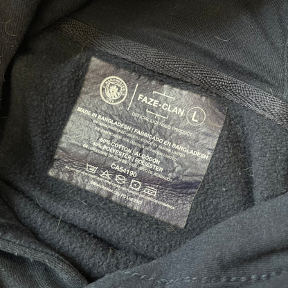 FaZe Clan x Manchester City 2019 Hoodie is an official collaboration combining esports and football culture. Made in Portugal from a 60% cotton and 40% polyester blend, it features the Manchester City club crest on the right chest and the FaZe Clan logo on the left. The back is finished with a large "FAZE CITY" graphic, with ribbed cuffs, a ribbed hem, and a kangaroo pocket.