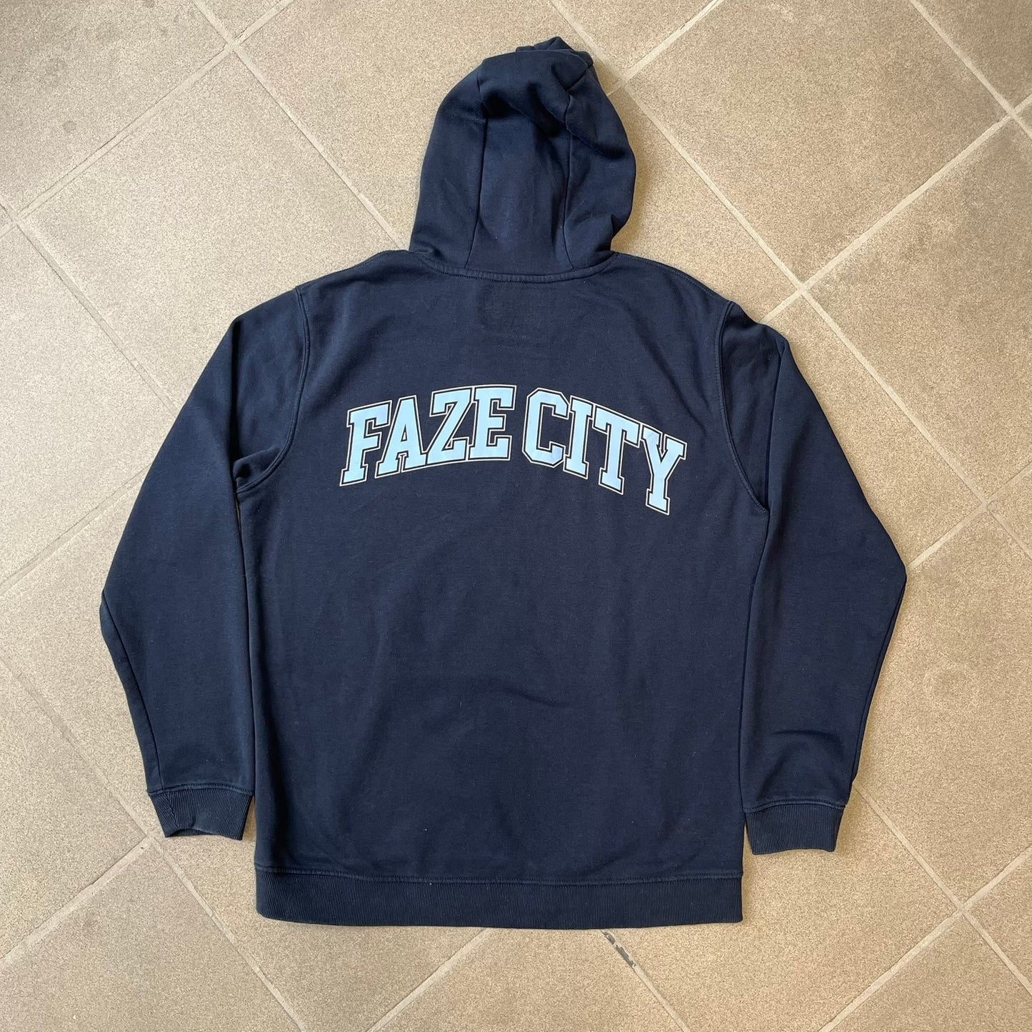 FaZe Clan x Manchester City 2019 Hoodie is an official collaboration combining esports and football culture. Made in Portugal from a 60% cotton and 40% polyester blend, it features the Manchester City club crest on the right chest and the FaZe Clan logo on the left. The back is finished with a large "FAZE CITY" graphic, with ribbed cuffs, a ribbed hem, and a kangaroo pocket.