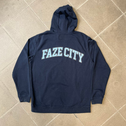 FaZe Clan x Manchester City 2019 Hoodie is an official collaboration combining esports and football culture. Made in Portugal from a 60% cotton and 40% polyester blend, it features the Manchester City club crest on the right chest and the FaZe Clan logo on the left. The back is finished with a large "FAZE CITY" graphic, with ribbed cuffs, a ribbed hem, and a kangaroo pocket.