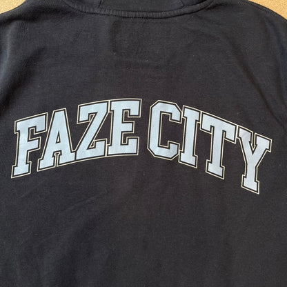 FaZe Clan x Manchester City 2019 Hoodie is an official collaboration combining esports and football culture. Made in Portugal from a 60% cotton and 40% polyester blend, it features the Manchester City club crest on the right chest and the FaZe Clan logo on the left. The back is finished with a large "FAZE CITY" graphic, with ribbed cuffs, a ribbed hem, and a kangaroo pocket.