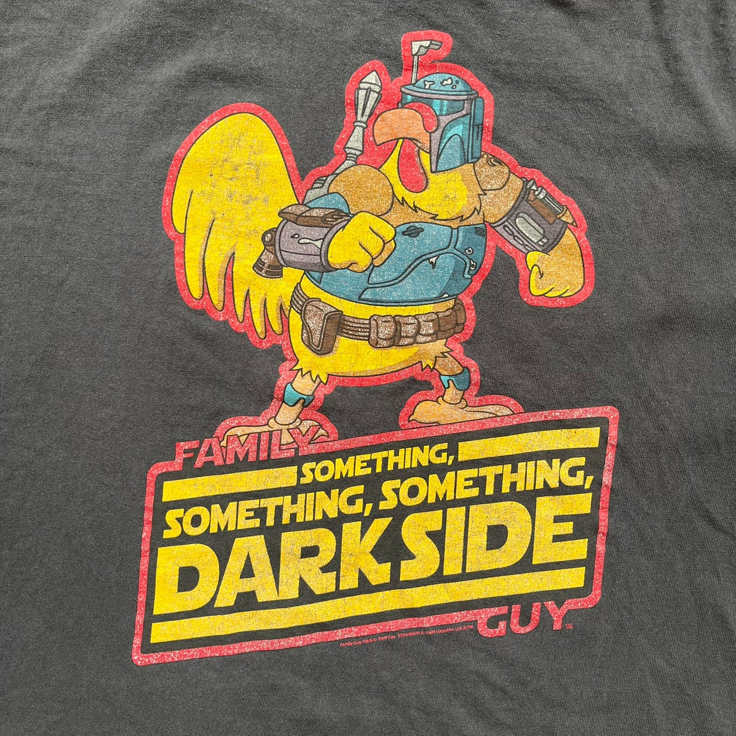Family Guy 2009 Star Wars "Something Darkside" Tee is a washed black T-shirt made on a Delta Pro Weight blank. The front features Ernie the Giant Chicken dressed as Boba Fett above yellow Star Wars-style “Something, Something, Something, Dark Side” text with a red Family Guy outline surrounding the graphic. Small 2009 licensing details are printed below the design.