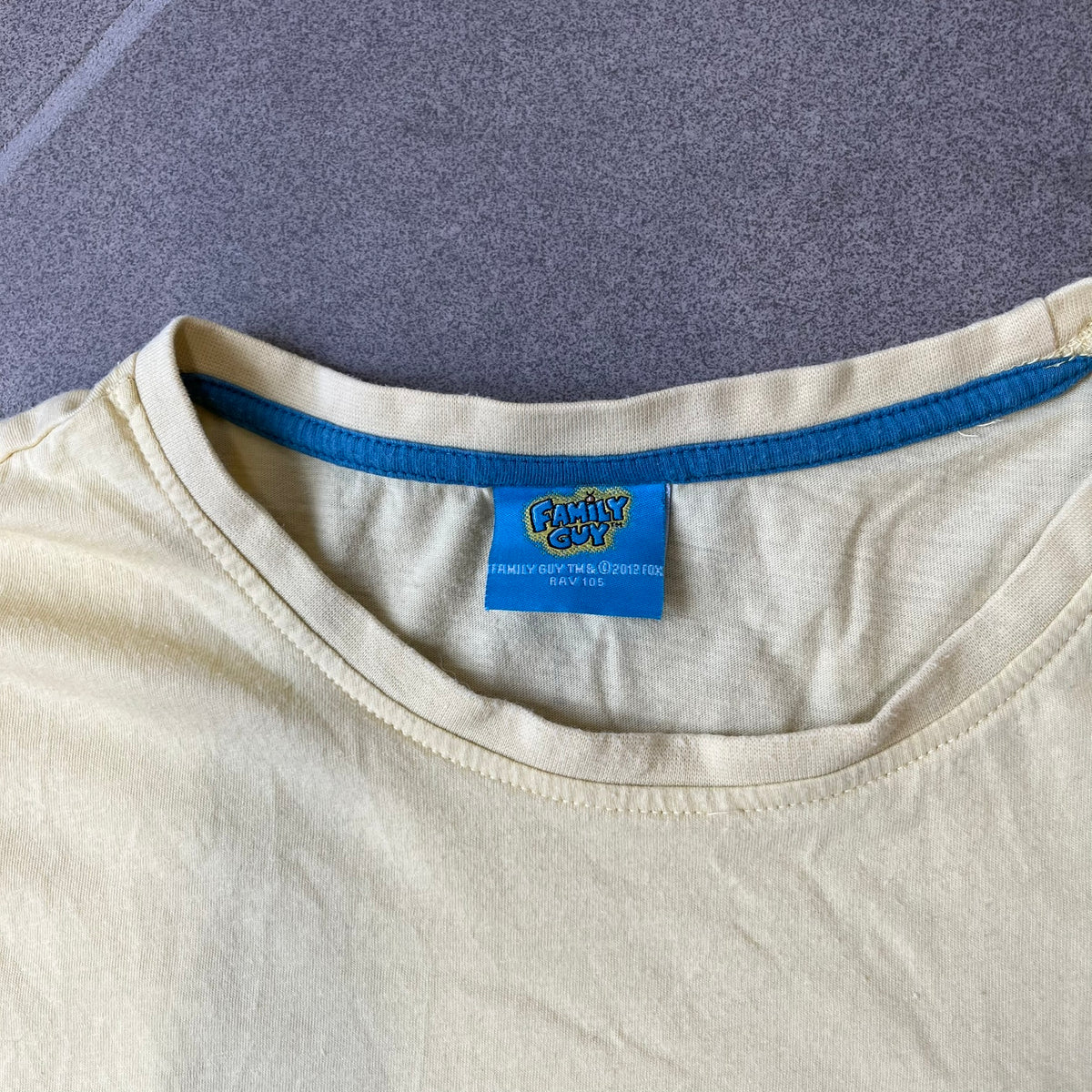 Family Guy 2012 Peter Griffin #1 Dad Tee features a yellow T-shirt with a front graphic of Peter Griffin wearing a helmet and elbow and knee protectors while running with a pair of scissors. A “#1 Dad” text is printed underneath the graphic. Includes a 2012 licensed neck tag.
