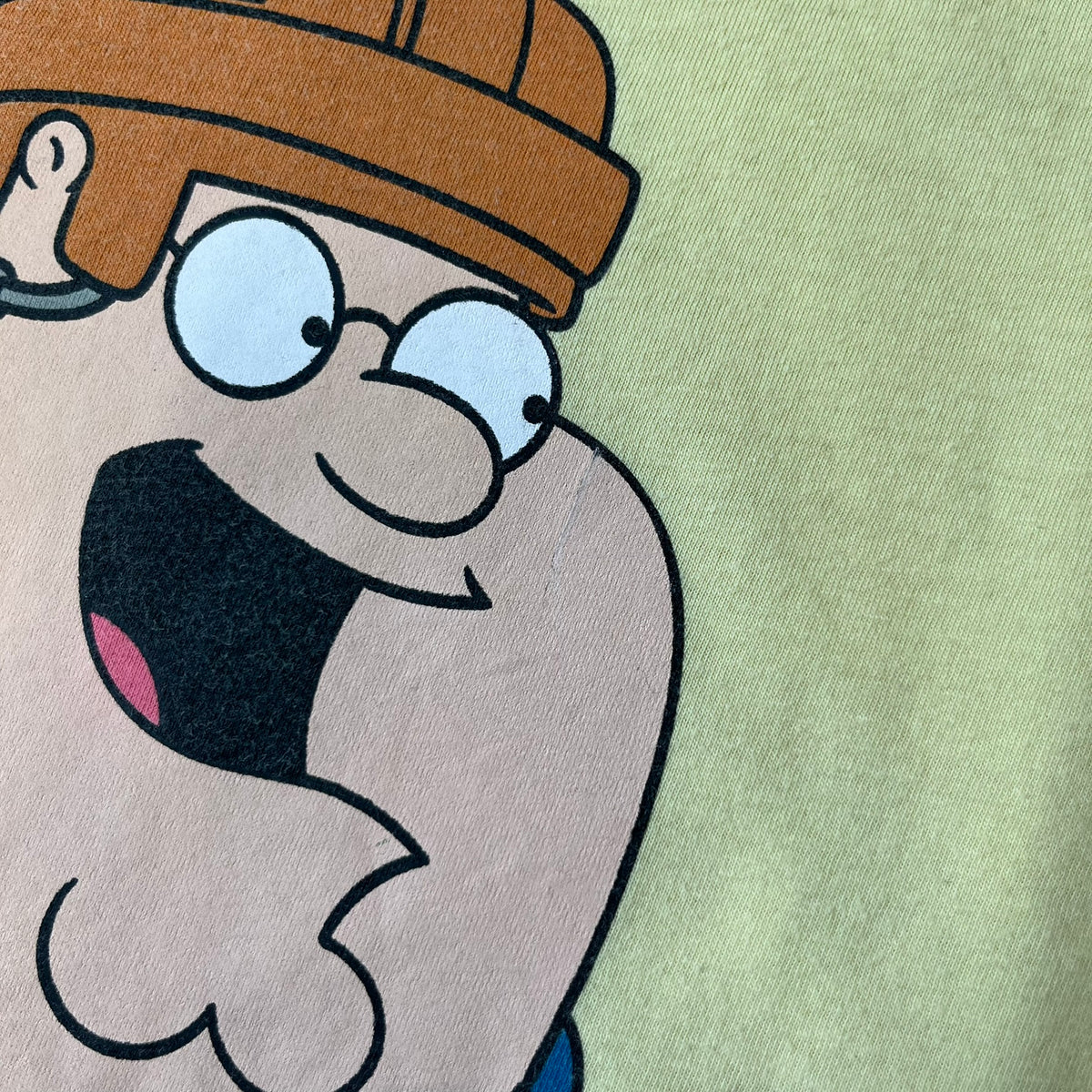 Family Guy 2012 Peter Griffin #1 Dad Tee features a yellow T-shirt with a front graphic of Peter Griffin wearing a helmet and elbow and knee protectors while running with a pair of scissors. A “#1 Dad” text is printed underneath the graphic. Includes a 2012 licensed neck tag.
