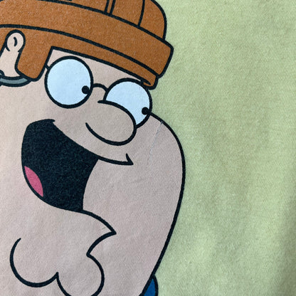 Family Guy 2012 Peter Griffin #1 Dad Tee features a yellow T-shirt with a front graphic of Peter Griffin wearing a helmet and elbow and knee protectors while running with a pair of scissors. A “#1 Dad” text is printed underneath the graphic. Includes a 2012 licensed neck tag.
