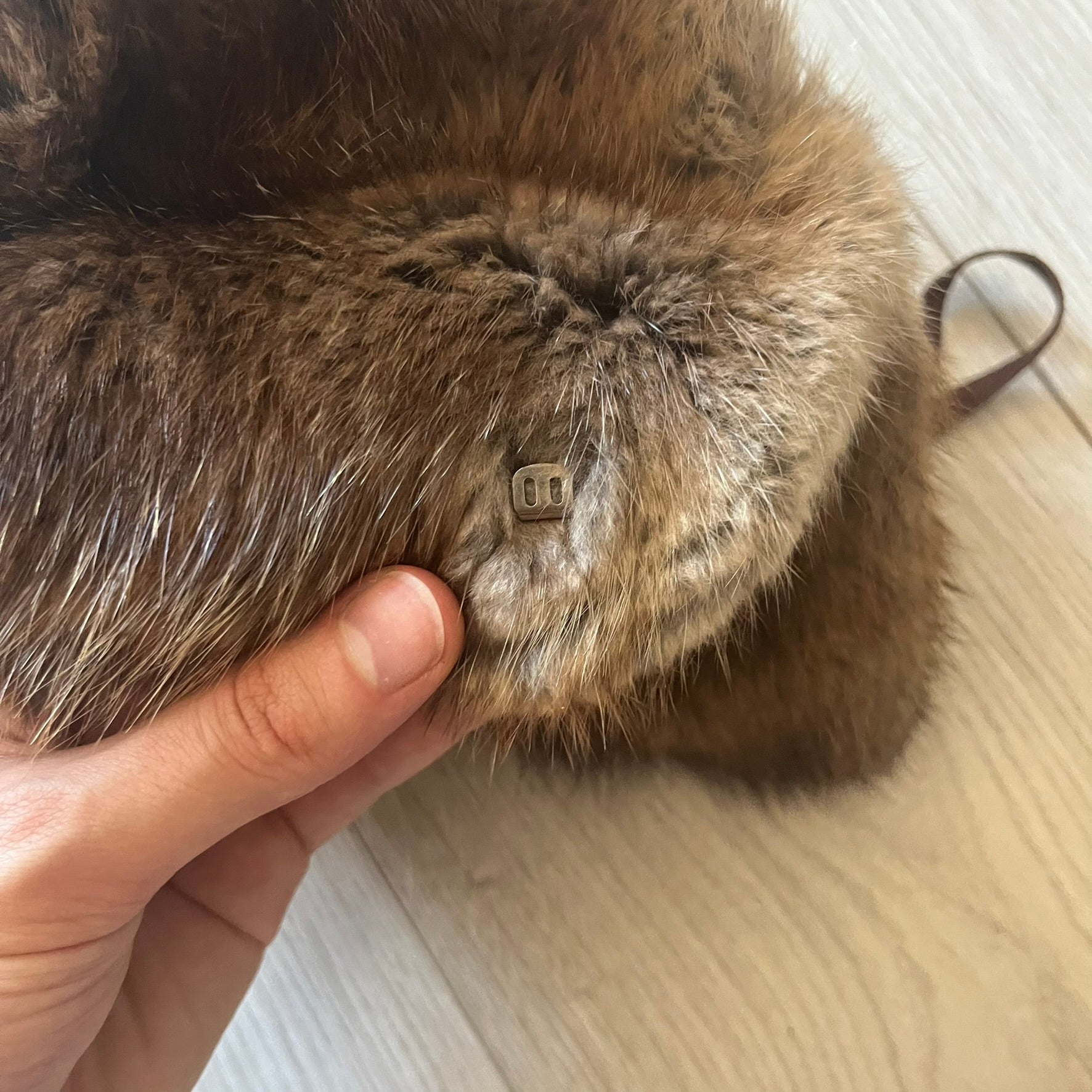 Fur ushanka hat featuring a Kulo tag inside and two leather tie strings. The front flap can be secured or folded back using small metal hooks for adjustable coverage. Designed for warmth and comfort, this classic winter piece offers both functionality and timeless style.