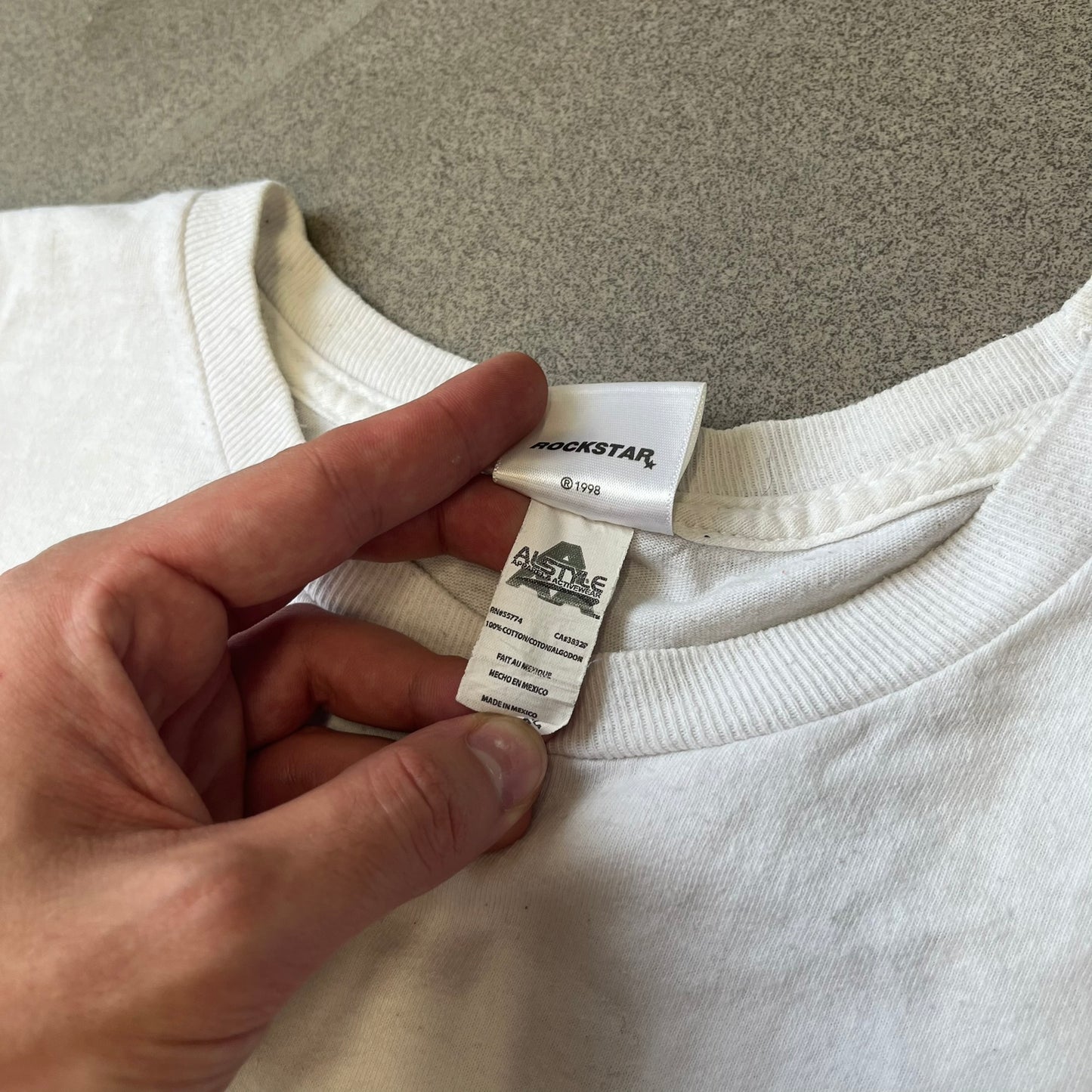 GTA V Los Santos 2013 White Tee features a white design with a large “Los Santos” graphic on the front in a tattoo-style font. The lower front includes a GTA V tag detail, while the neck tag features the Rockstar logo. The back has a small black Rockstar logo.
