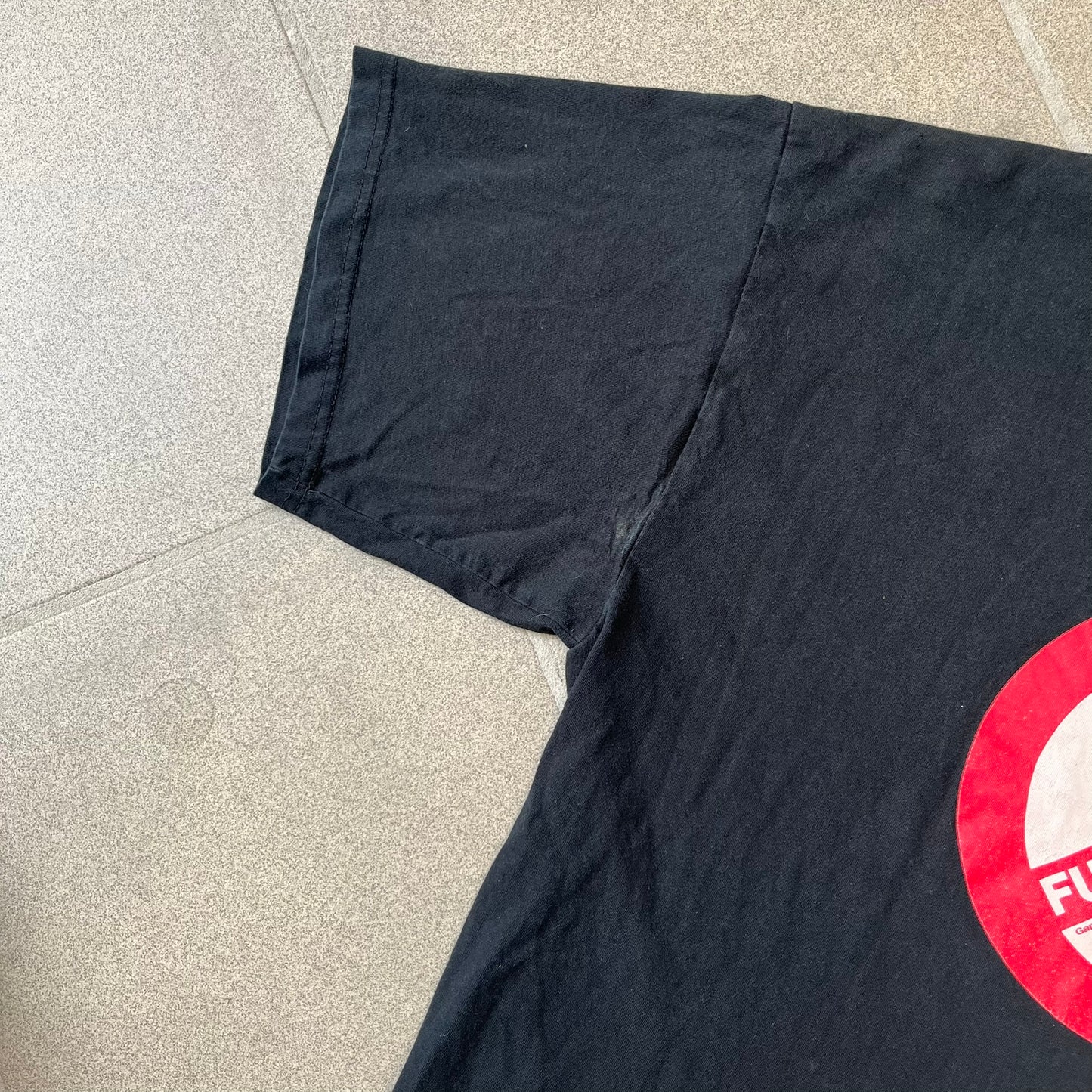 GamersWear 2010's Fuck The Sun Black Tee features a black 100% cotton T-shirt with a road sign-style graphic on the front. The graphic shows a black figure sitting at a computer beneath a black sun, surrounded by a white background and red outline. A red line crosses the design with white “Fuck The Sun” text, along with small red GamersWear branding.
