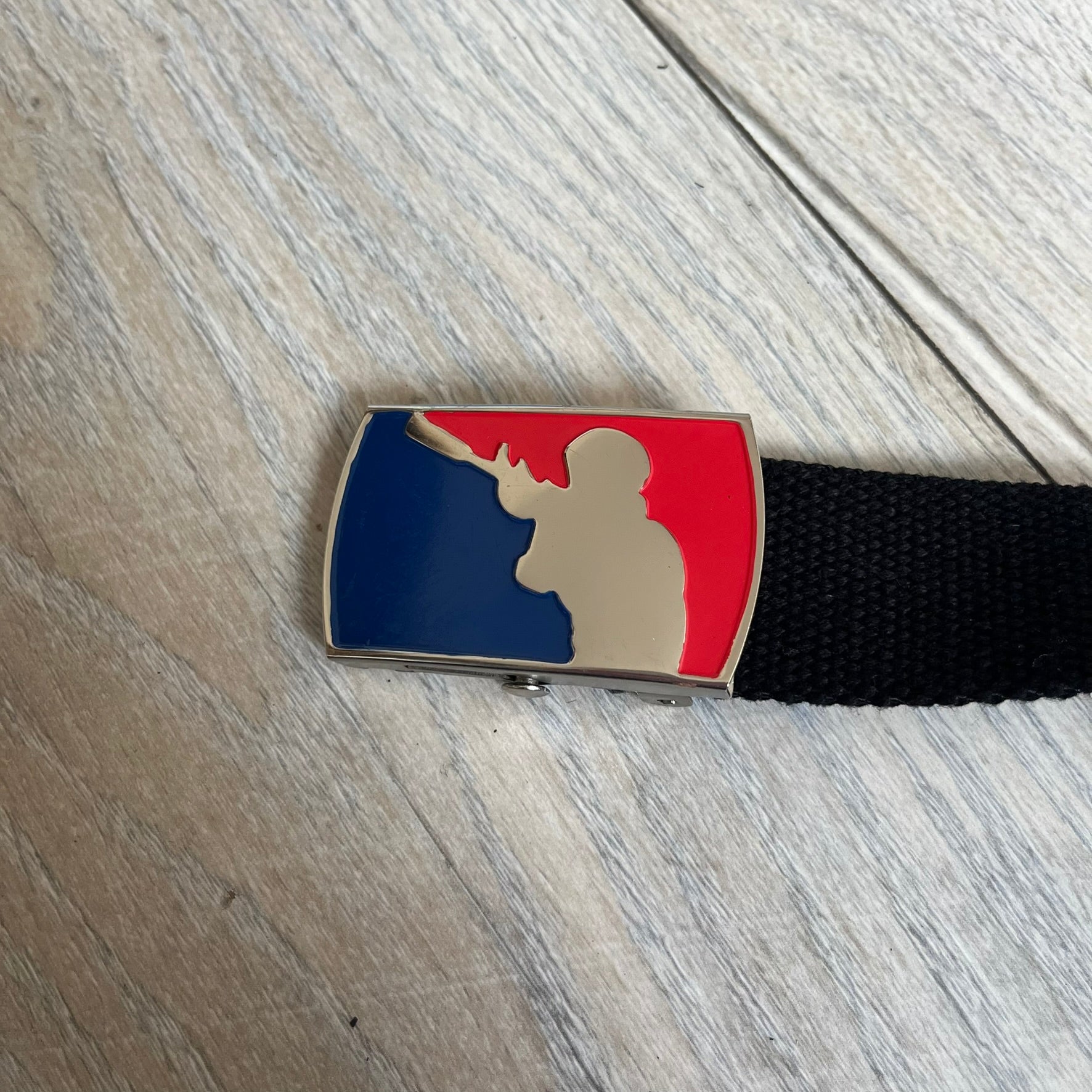 Gamerswear Counter-Strike 2016 Black Belt is a black cotton belt with an adjustable fit and a metal tip featuring a cutout Gamerswear logo. The buckle showcases an armed character in a silver finish, framed by blue enamel on the left side and red enamel on the right. The central figure is highlighted with a raised silver design and matching silver border detailing.