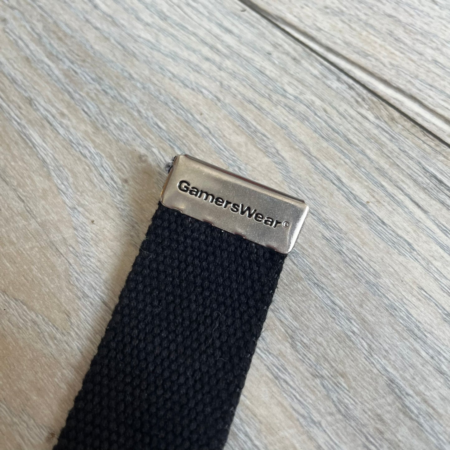 Gamerswear Counter-Strike 2016 Black Belt is a black cotton belt with an adjustable fit and a metal tip featuring a cutout Gamerswear logo. The buckle showcases an armed character in a silver finish, framed by blue enamel on the left side and red enamel on the right. The central figure is highlighted with a raised silver design and matching silver border detailing.