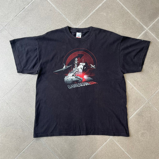 Gamescom 2014 WOT, Warplanes & Warships Promo Tee features a black 100% cotton T-shirt made on a Screen Stars blank. The front has a white and red graphic depicting a plane, tank, and warship, with “gamescom 2014” text underneath. The upper back has World of Tanks, World of Warplanes, and World of Warships logos, while the sleeve features a Wargaming.net logo.
