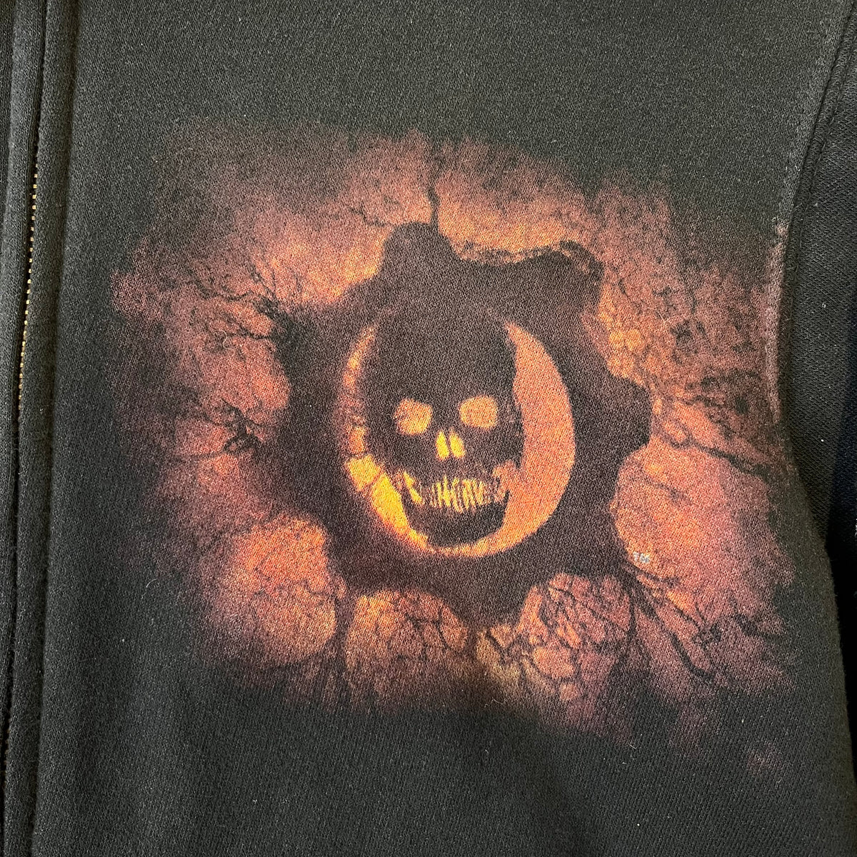 Gears of War 3 Marcus Fenix 2010 Promo Hoodie is a black zip-up hoodie with a dark Crimson Omen logo in orange tones on the left upper chest and a bloody Delta-One logo on one sleeve. The back features a large Marcus Fenix graphic with “Gears of War 3” text below it and a small 2010 Epic Games licensing mark.